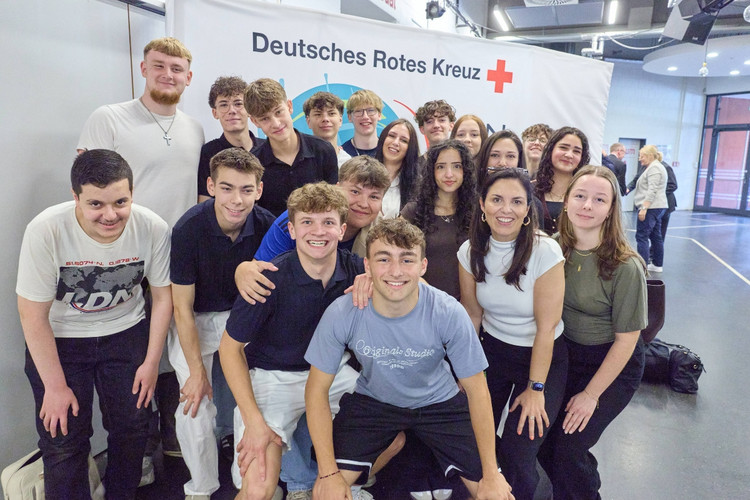 Eine Schulklasse posiert vor einem JRK-Logo zum Gruppenbild